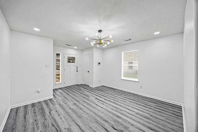 spare room featuring baseboards, visible vents, wood finished floors, a textured ceiling, and a notable chandelier