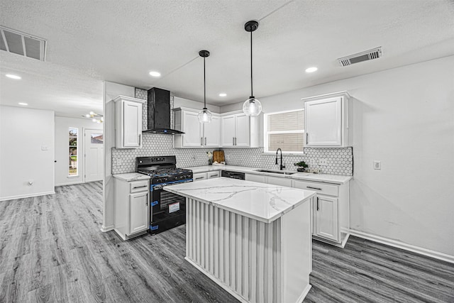 kitchen with wall chimney range hood, a center island, white cabinetry, and gas stove