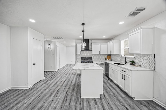 kitchen featuring a sink, a kitchen island, visible vents, white cabinets, and wall chimney range hood