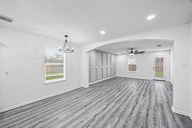 unfurnished living room with visible vents, a textured ceiling, arched walkways, and wood finished floors