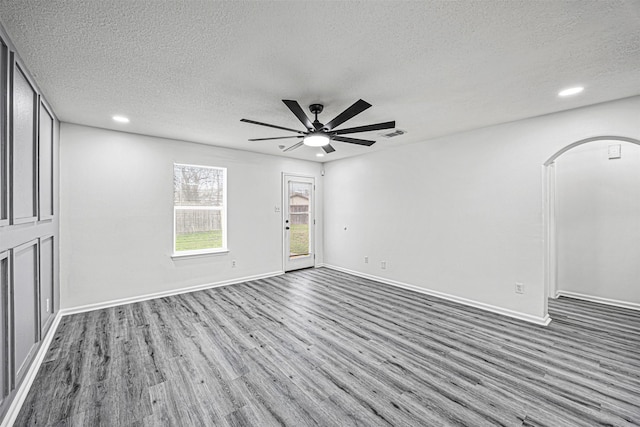 unfurnished room with visible vents, arched walkways, a ceiling fan, baseboards, and wood finished floors