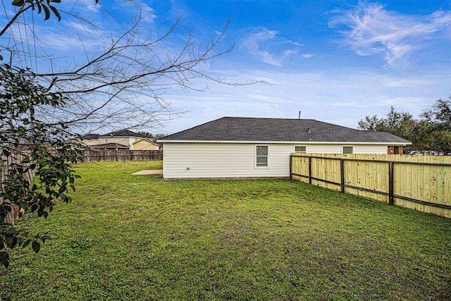 rear view of house with a fenced backyard, roof with shingles, and a yard