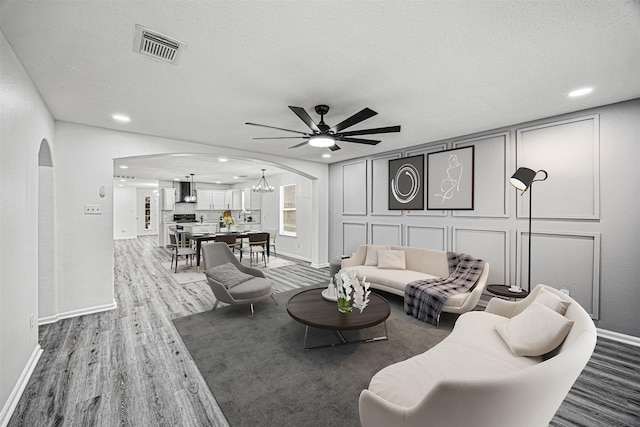 living area with visible vents, arched walkways, wood finished floors, a decorative wall, and ceiling fan with notable chandelier