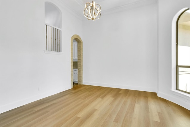 empty room with ornamental molding, a notable chandelier, and light hardwood / wood-style floors