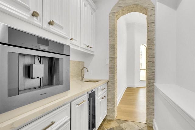 kitchen with white cabinetry, sink, beverage cooler, and stainless steel oven