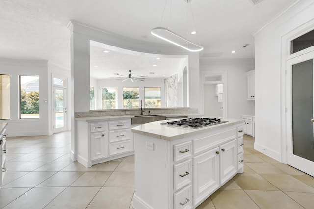 kitchen featuring stainless steel gas cooktop, sink, light tile patterned floors, a kitchen island, and white cabinets