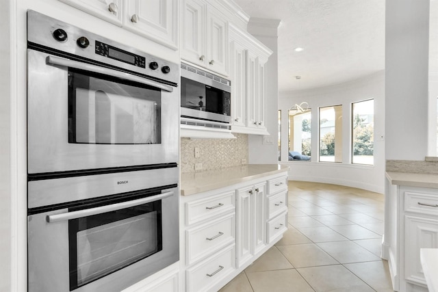 kitchen with stainless steel appliances, white cabinetry, light tile patterned floors, and backsplash