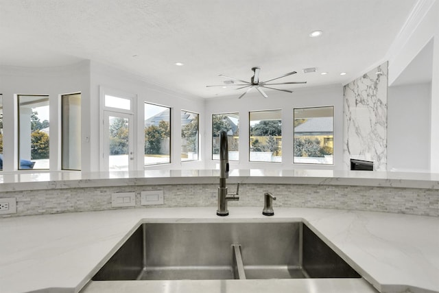 room details with tasteful backsplash, ornamental molding, light stone countertops, and sink