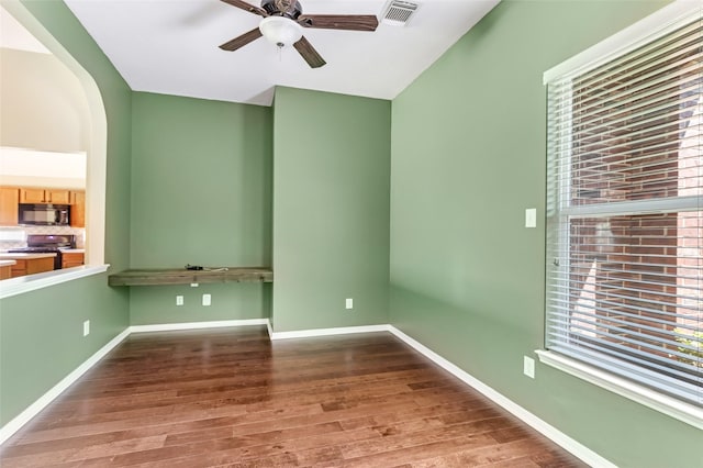 unfurnished room featuring arched walkways, a ceiling fan, visible vents, wood finished floors, and baseboards