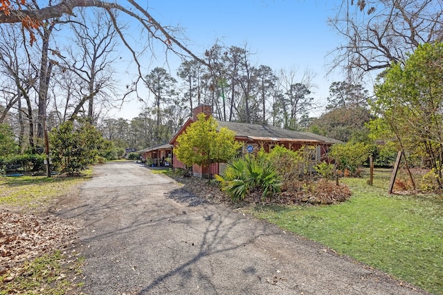 exterior space featuring a chimney, aphalt driveway, and a yard