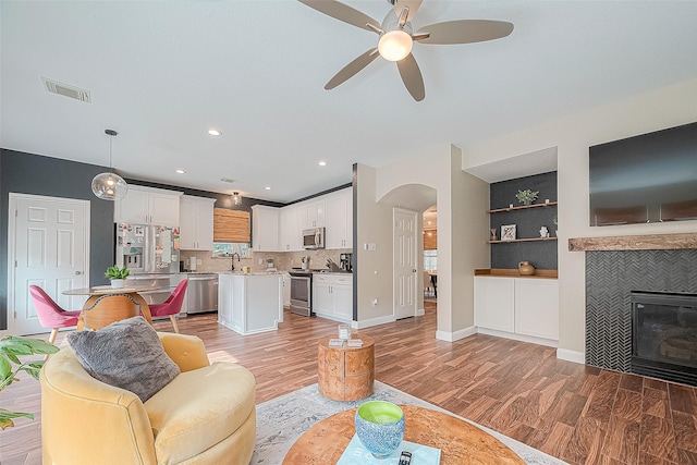 living room featuring built in shelves, sink, light hardwood / wood-style flooring, a tile fireplace, and ceiling fan