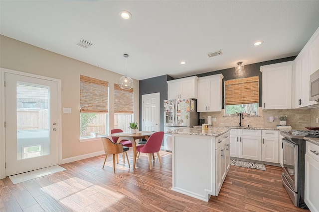 kitchen with sink, white cabinetry, a center island, hanging light fixtures, and stainless steel appliances