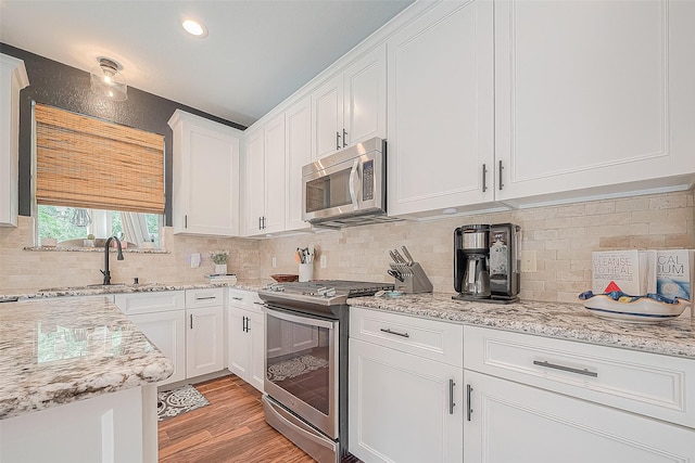 kitchen with white cabinetry, stainless steel appliances, light stone counters, tasteful backsplash, and light wood-type flooring