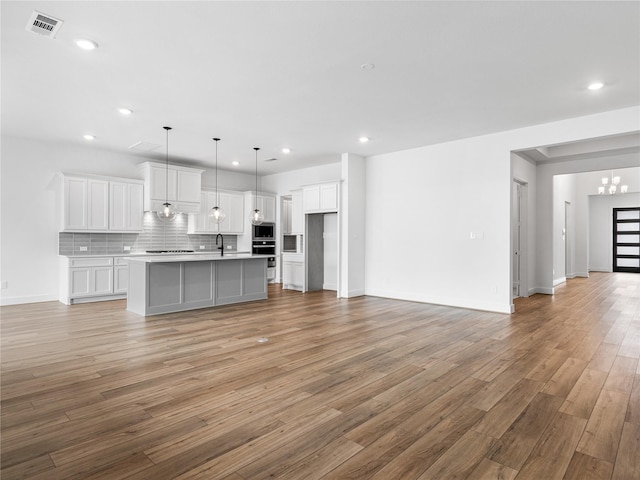 kitchen with a notable chandelier, tasteful backsplash, a center island with sink, and white cabinets