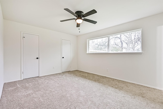 unfurnished bedroom featuring multiple closets, light colored carpet, and ceiling fan