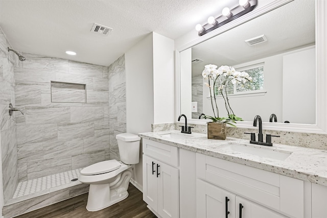 bathroom featuring hardwood / wood-style floors, tiled shower, vanity, a textured ceiling, and toilet