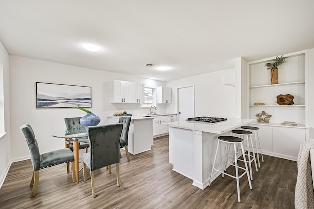 kitchen featuring a breakfast bar, a center island, light stone countertops, white cabinets, and dark hardwood / wood-style flooring