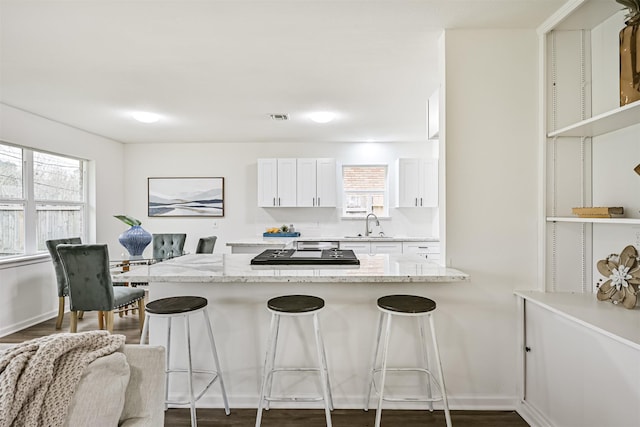 kitchen with light stone countertops, a breakfast bar, a wealth of natural light, and white cabinets