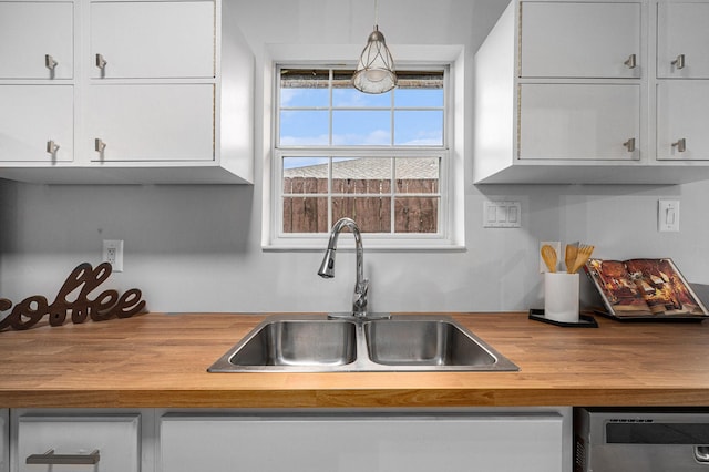 kitchen with pendant lighting, sink, butcher block countertops, dishwasher, and white cabinetry