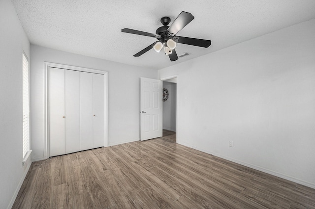 unfurnished bedroom with ceiling fan, a closet, hardwood / wood-style floors, and a textured ceiling