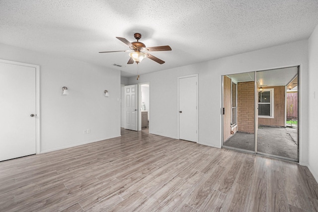 unfurnished bedroom featuring ceiling fan, multiple closets, light hardwood / wood-style floors, and a textured ceiling