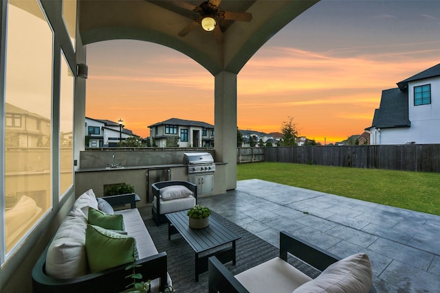 patio terrace at dusk with ceiling fan, area for grilling, a yard, and outdoor lounge area