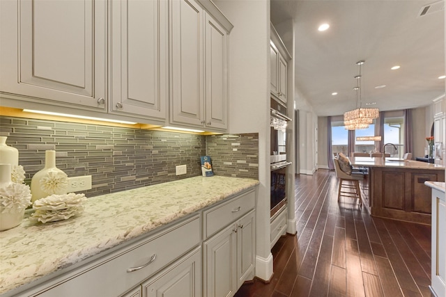 kitchen featuring dark hardwood / wood-style floors, sink, decorative backsplash, hanging light fixtures, and light stone countertops