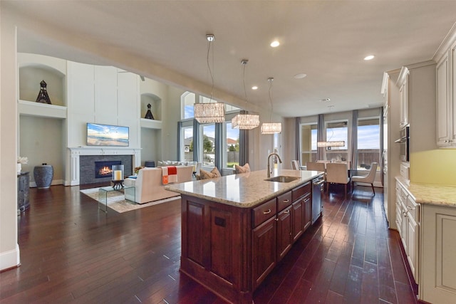 kitchen with built in shelves, sink, light stone counters, decorative light fixtures, and an island with sink