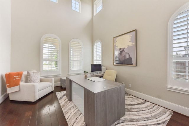 office featuring a healthy amount of sunlight, dark wood-type flooring, and a towering ceiling