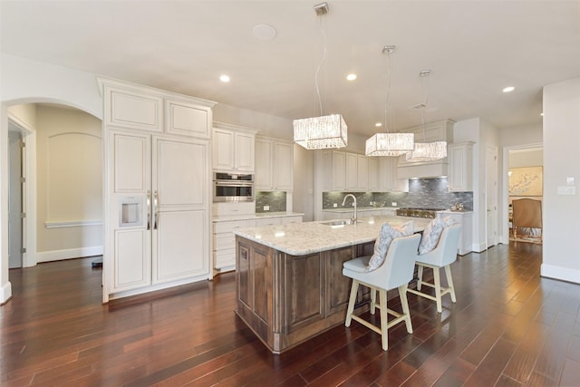 kitchen with pendant lighting, sink, a kitchen island with sink, light stone countertops, and oven