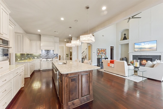 kitchen with premium range hood, sink, decorative light fixtures, a kitchen island with sink, and white cabinets