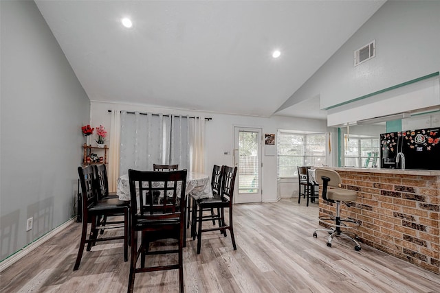 dining space with bar area, high vaulted ceiling, and light hardwood / wood-style flooring