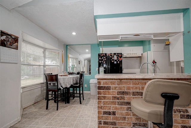 kitchen with white cabinetry, sink, a textured ceiling, and black fridge