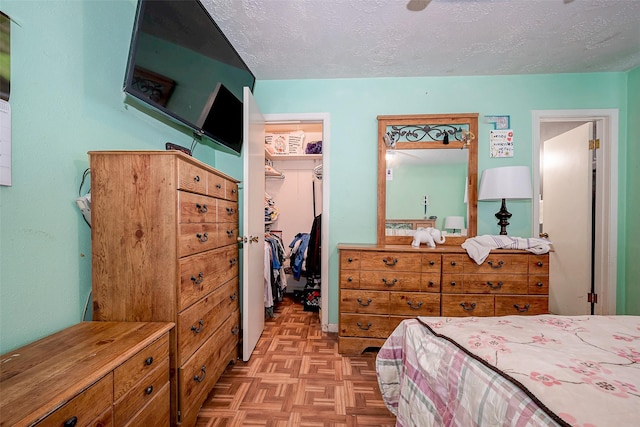 bedroom with a textured ceiling, a walk in closet, a closet, and light parquet flooring