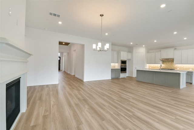 16119 Rustling Woods Rd, Conroe, TX 77302 - kitchen featuring a glass covered fireplace, a chandelier, decorative backsplash, light wood-type flooring, and white cabinetry
