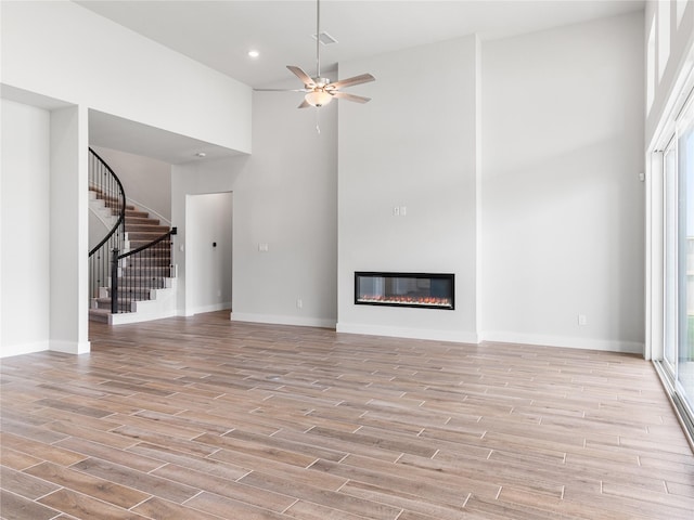 10903 Providence Ct, Missouri City, TX 77459 - unfurnished living room featuring a high ceiling, a ceiling fan, light wood finished floors, stairs, and a glass covered fireplace