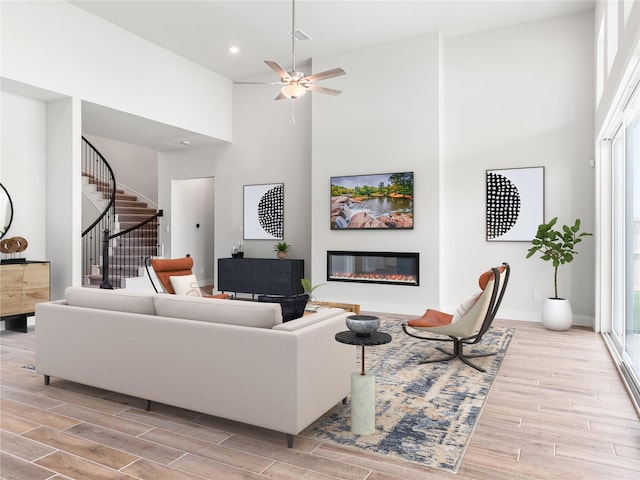 10903 Providence Ct, Missouri City, TX 77459 - living area featuring wood finished floors, a glass covered fireplace, a high ceiling, stairs, and ceiling fan