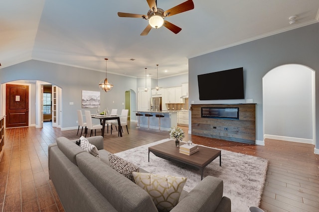 living room featuring baseboards, wood-type flooring, arched walkways, and crown molding