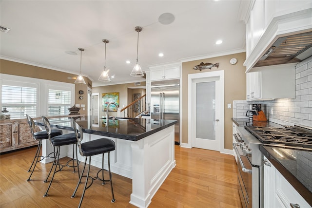 kitchen featuring white cabinets, a kitchen bar, premium appliances, custom range hood, and a center island with sink