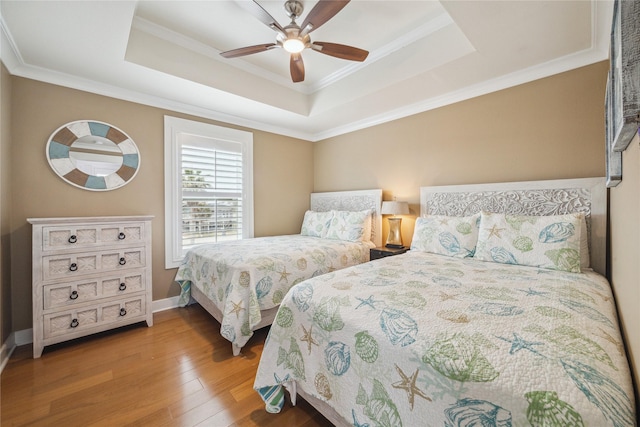 bedroom with ceiling fan, ornamental molding, wood-type flooring, and a raised ceiling