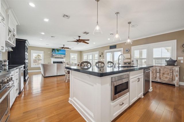 kitchen featuring stainless steel microwave, an island with sink, sink, white cabinets, and light hardwood / wood-style flooring