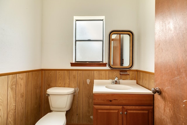 bathroom featuring vanity, wooden walls, and toilet