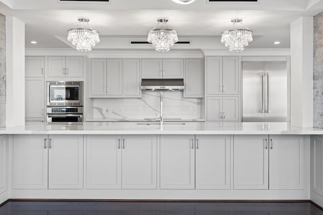 kitchen featuring white cabinetry, built in appliances, a notable chandelier, and pendant lighting