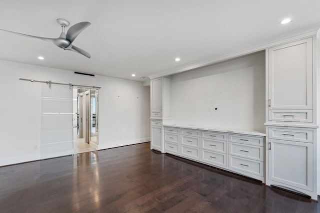 interior space featuring dark wood-type flooring, ceiling fan, and a barn door