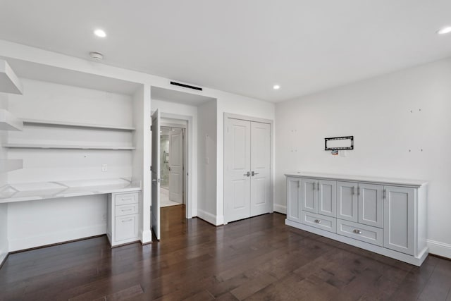 unfurnished bedroom with dark wood-type flooring, built in desk, and a closet