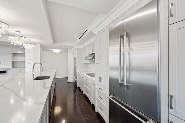 kitchen featuring stainless steel appliances, light stone counters, pendant lighting, sink, and white cabinetry