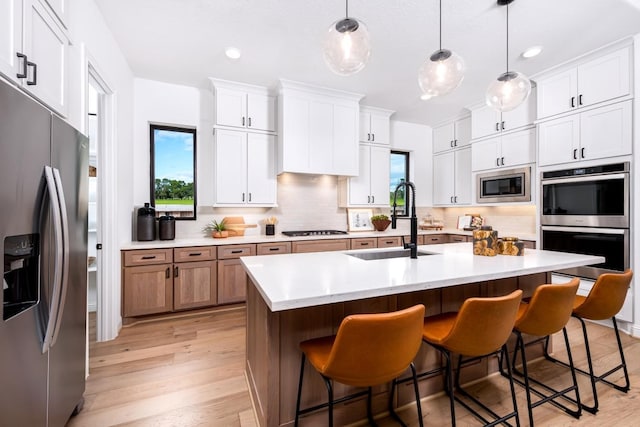 kitchen featuring sink, hanging light fixtures, stainless steel appliances, an island with sink, and white cabinets