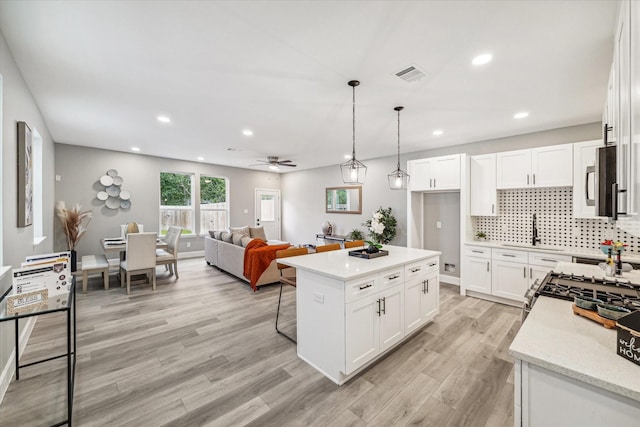 kitchen featuring pendant lighting, white cabinetry, a center island, tasteful backsplash, and light stone countertops