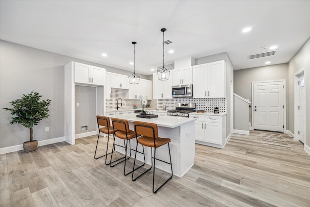 kitchen with stainless steel appliances, decorative light fixtures, a center island, and white cabinets