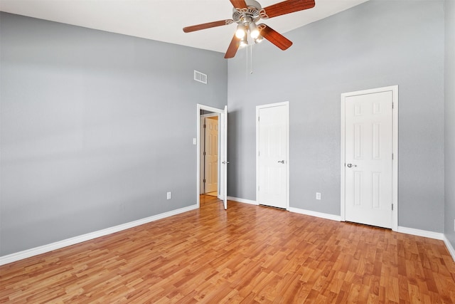 unfurnished bedroom featuring light wood finished floors, baseboards, visible vents, a ceiling fan, and a towering ceiling